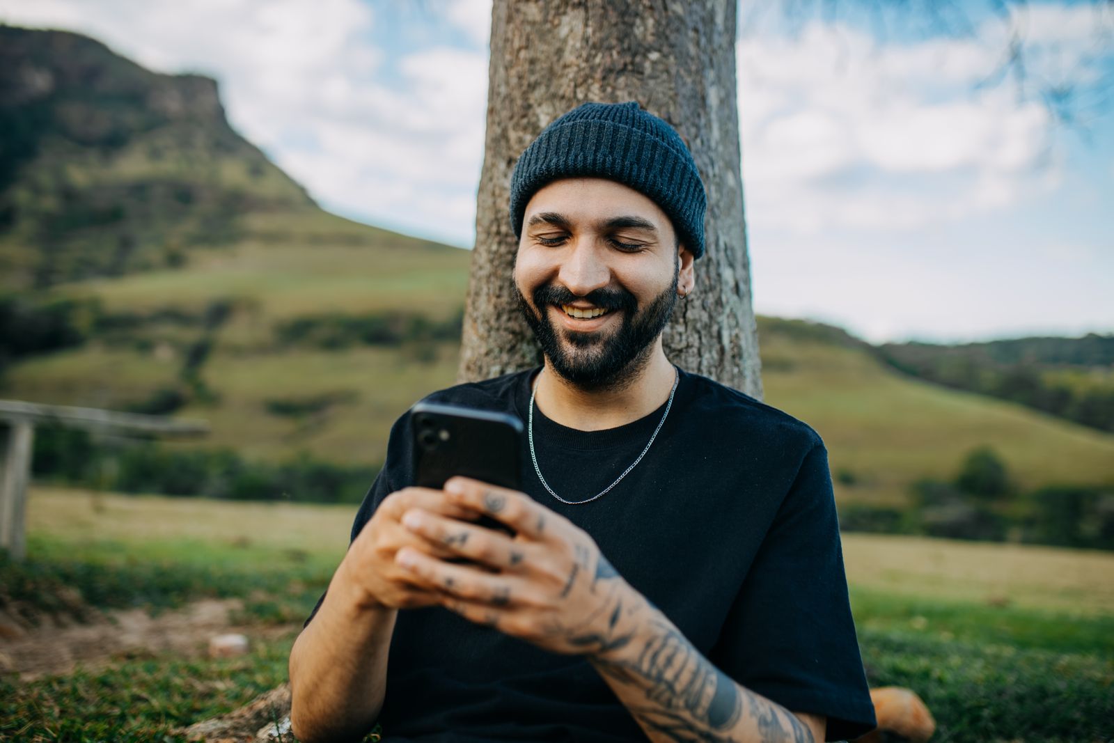 Un homme souriant écrit sur son téléphone, assis en extérieur