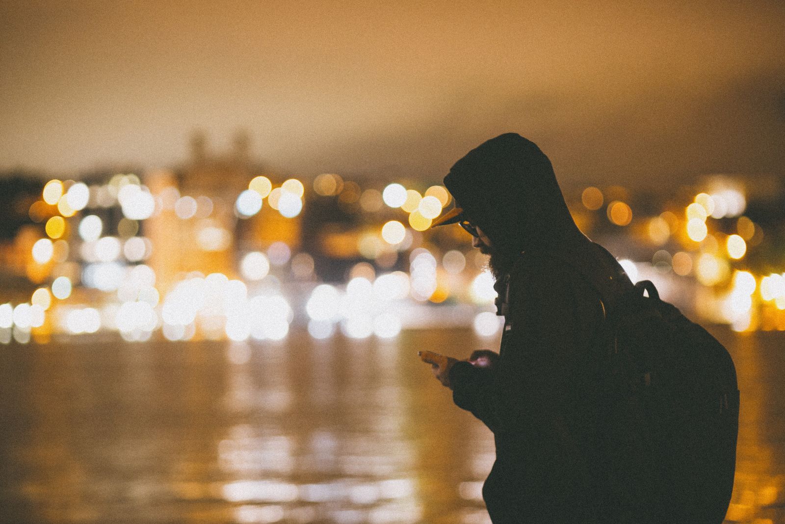 La silhouette d’un homme qui regarde son téléphone au bord d’un fleuve, la nuit